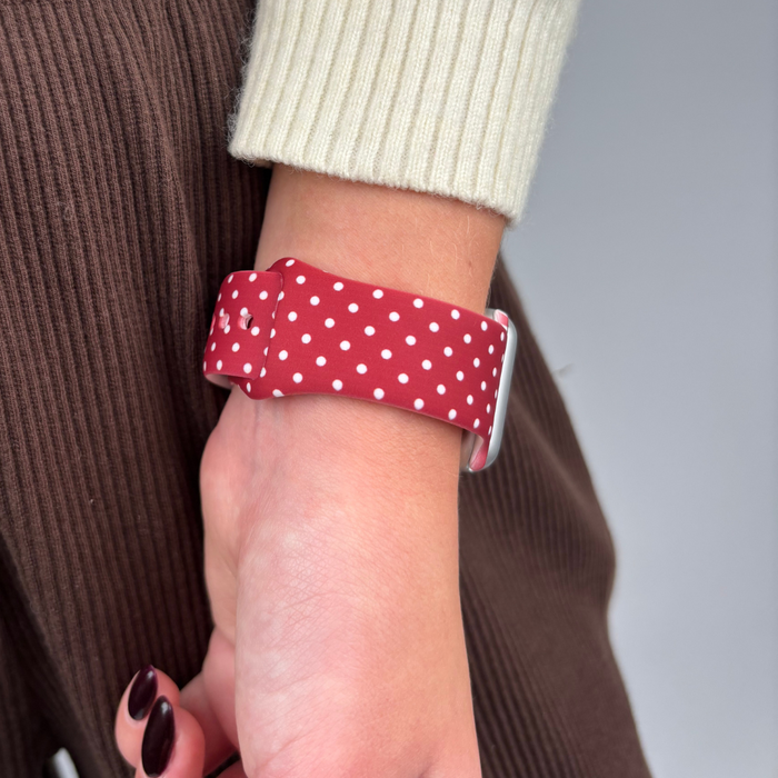 Burgundy polka dot Apple Watch strap on a wrist, paired with brown ribbed pants and a cream sweater.