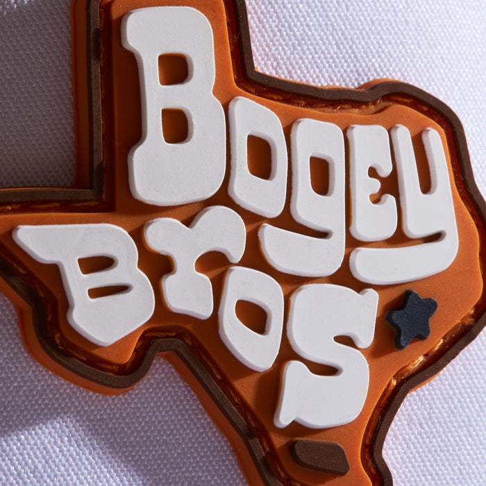 An orange Texas-shaped pin with bold, white letters spelling BOGEY BROS and a black star near the bottom right, sits on a textured white surface.