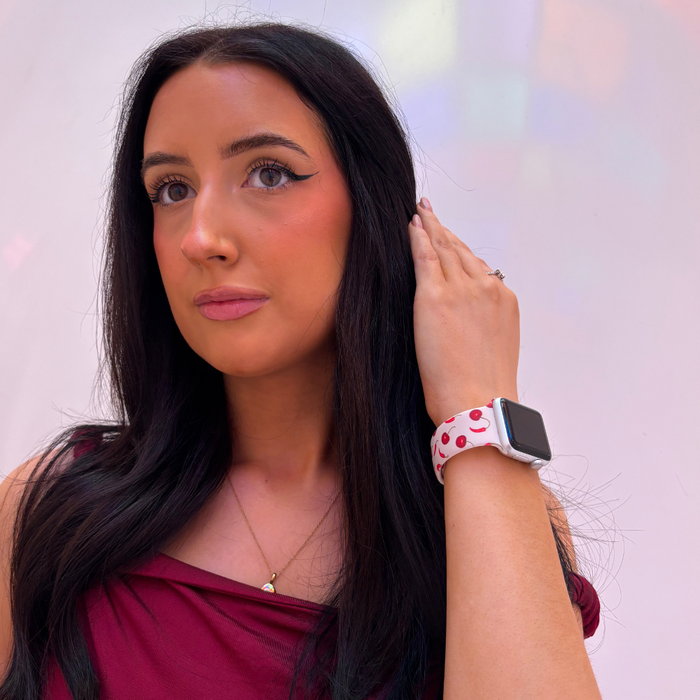 Woman in maroon top shows Coconut Lane Cherry Spice Apple Watch strap featuring a red and white cherry print.