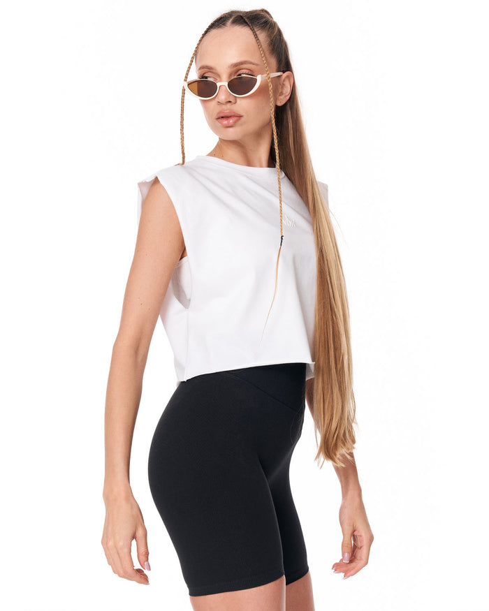 A woman modeling a sleeveless white top and black biker shorts against a plain white background.