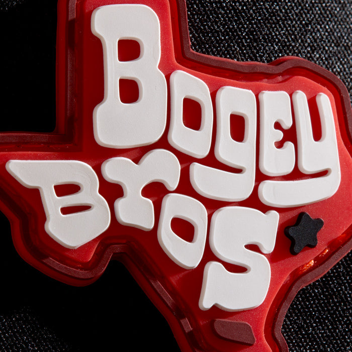 A red Texas-shaped badge with white, playful text saying “BOGEY BROS” and a small black star in the bottom right. The badge is set against a dark textured background.