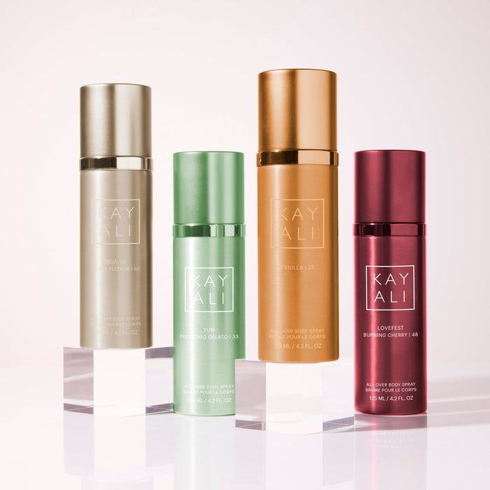 Four bottles of Kayali products on a reflective surface with a light background