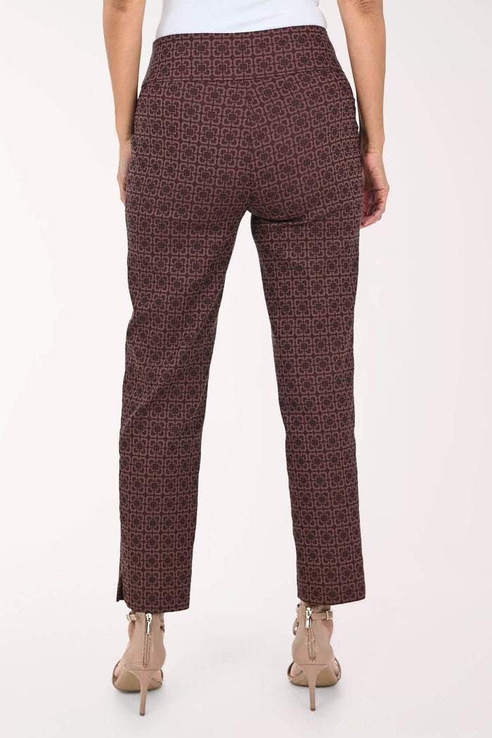 Back view of a person wearing slim-fit trousers with a dark brown and black geometric pattern, paired with beige high-heeled sandals against a plain white background.