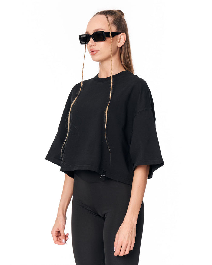 A woman modeling a black cropped short-sleeve top with wide draped sleeves and matching black leggings against a plain white background.