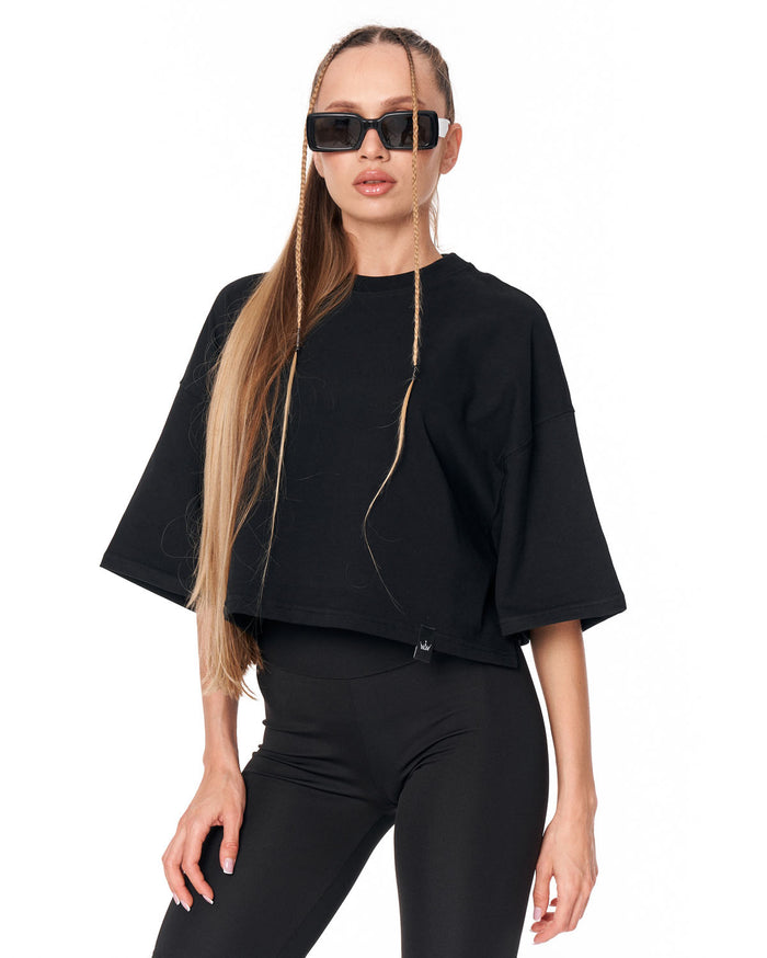 A woman modeling a black cropped tunic top with wide short sleeves and a drawstring neckline, paired with black leggings, against a plain white background.