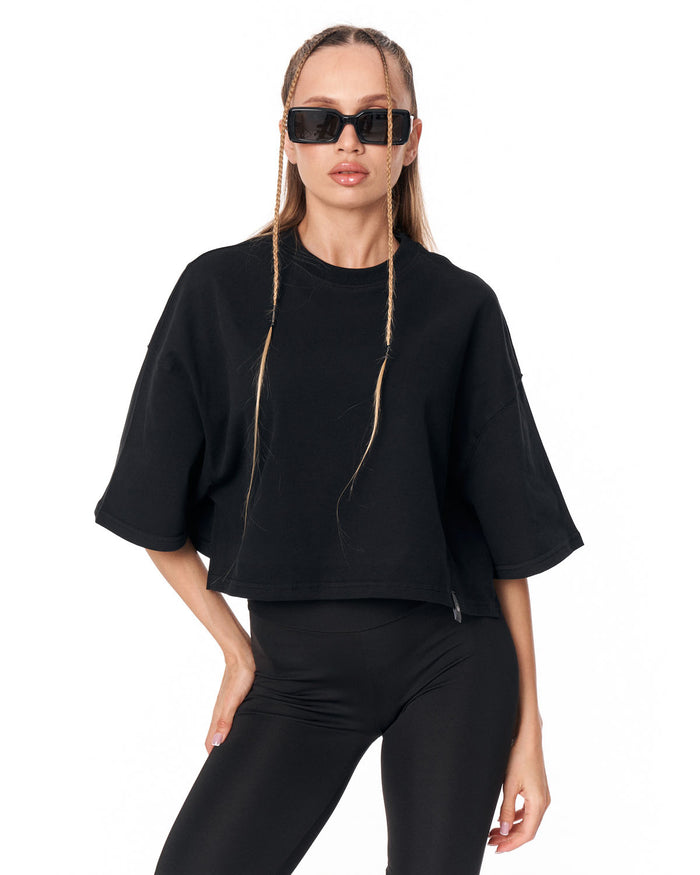 A model wearing a black cropped short-sleeve t-shirt and black leggings, styled with black sunglasses, against a plain white background.