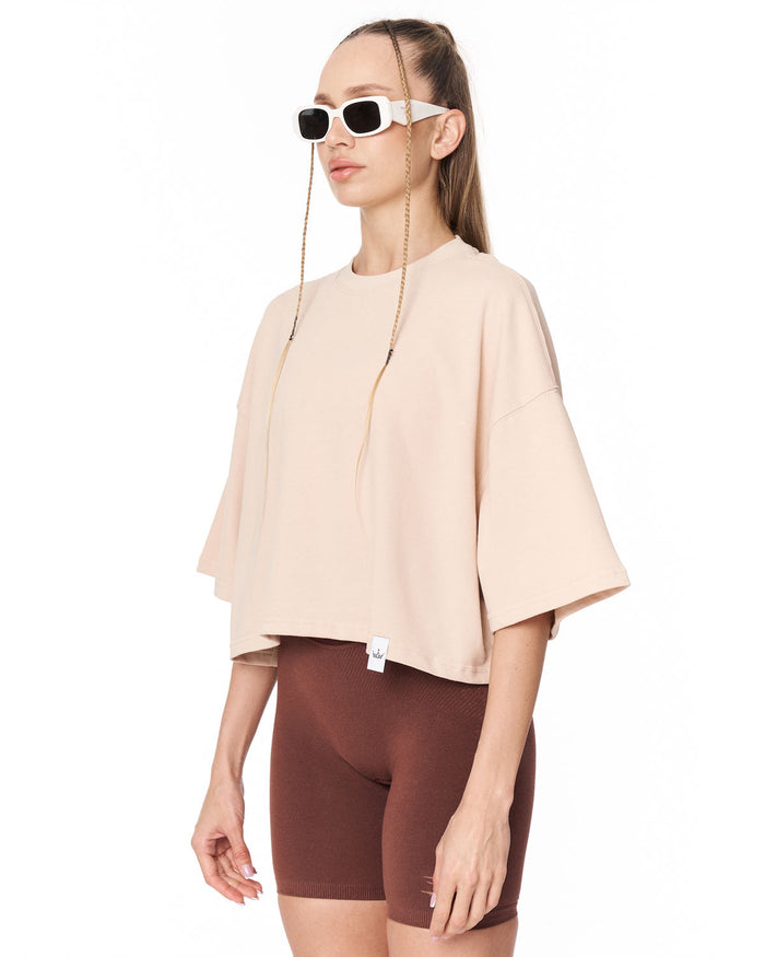 A woman modeling a light beige oversized short-sleeve top with brown fitted biker shorts against a plain white background.