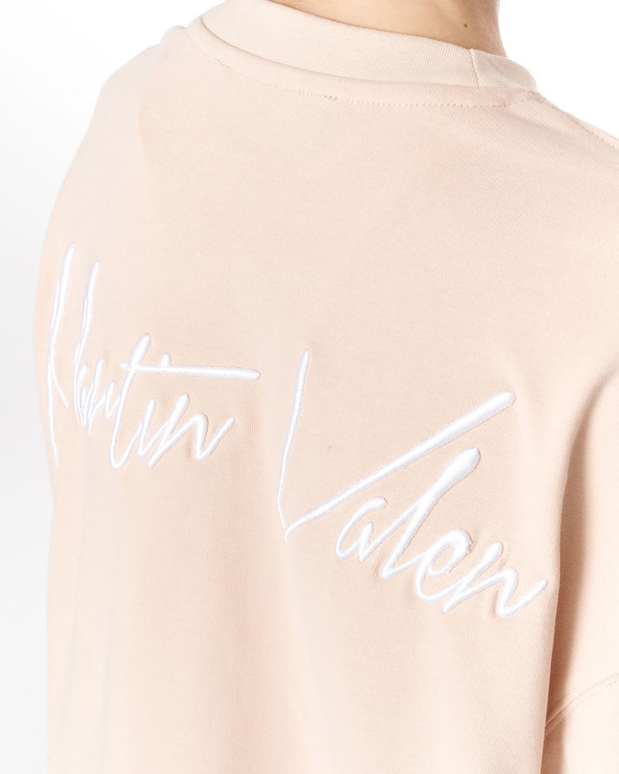 Close-up of the back of a light beige crewneck sweatshirt featuring a large white embroidered 'Martin Valen' logo across the back.