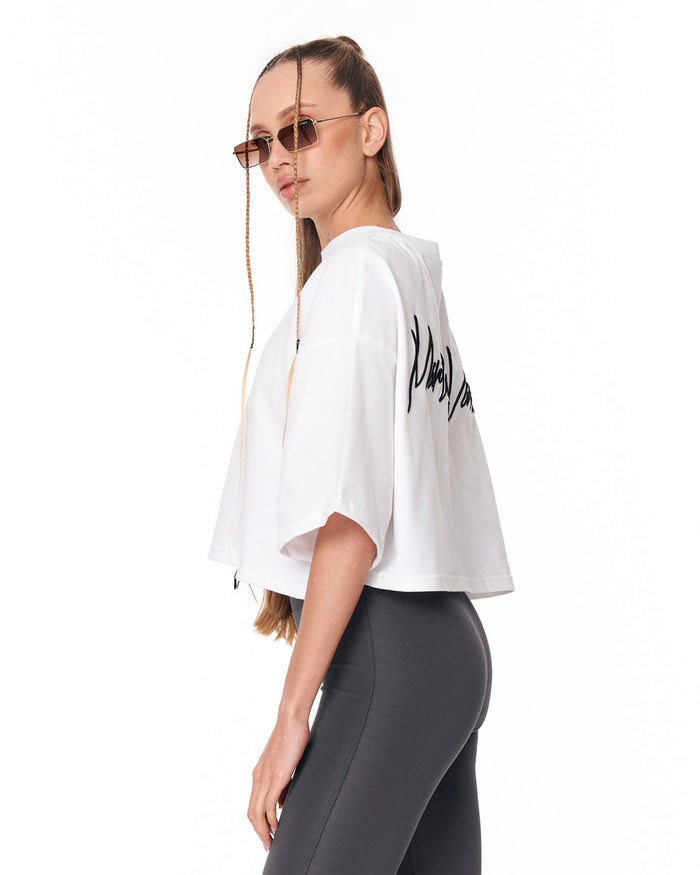 A woman wearing a white cropped t-shirt with black script text on the back, paired with dark gray leggings, photographed against a solid white background.