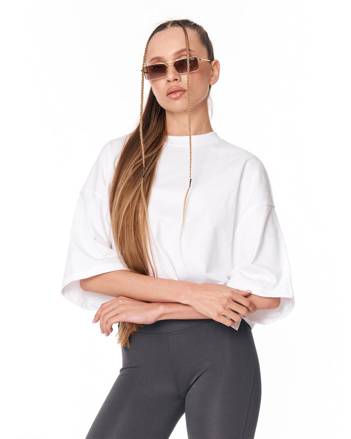 A woman modeling a white short-sleeve top with wide bell sleeves and dark gray leggings against a plain white background.
