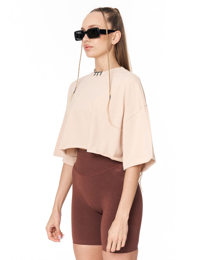 A woman modeling a light beige short-sleeve crop top and brown fitted bike shorts against a plain white background.