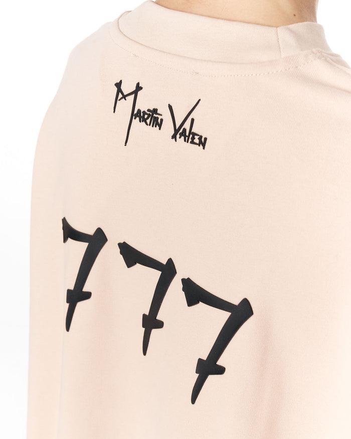 Close-up of the back of a light beige or cream t-shirt featuring a black Martin Valen signature logo near the collar and a large black '777' graphic below it.