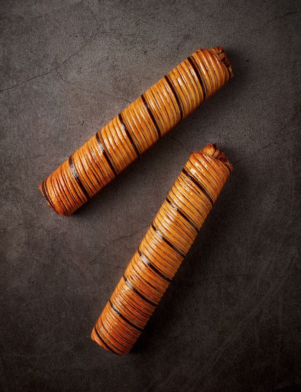 Two cylindrical pastries with woven patterns on a dark surface