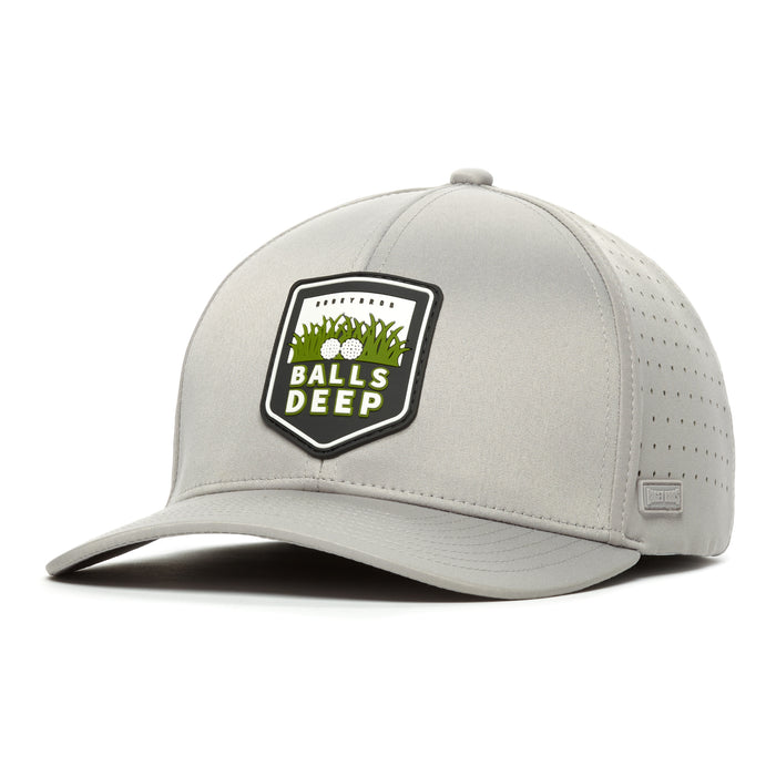 The Bogey Bros Balls Deep - Performance Golf Hat features a light gray design with a structured brim, perforated sides, and a stretch-fit band. The front patch displays grass, golf balls, and "BALLS DEEP" in bold white on a black shield.
