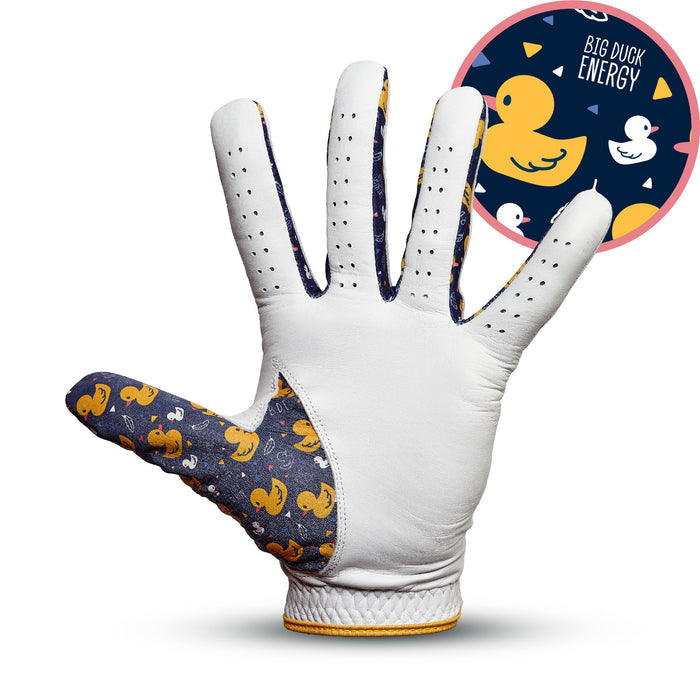 The Big Duck Energy - Glove is a white cabretta leather golf glove with a blue inner thumb and palm patterned with yellow rubber ducks. Beside it is a circular graphic showing the same duck pattern and "BIG DUCK ENERGY" in white text.