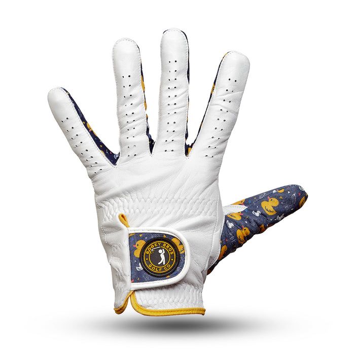 The Big Duck Energy - Glove is a white cabretta leather golf glove with finger and palm perforations, a navy thumb and inner wrist featuring yellow duck illustrations, and a “Birdie Town Golf Co.” patch with bird logo on the cuff.