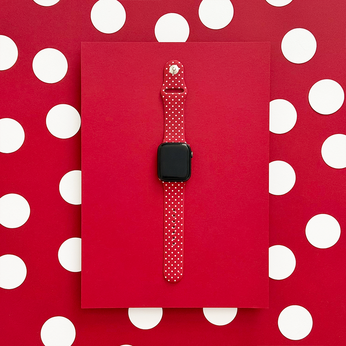 Burgundy Apple Watch strap with white polka dots, displayed on a red and white polka dot background.