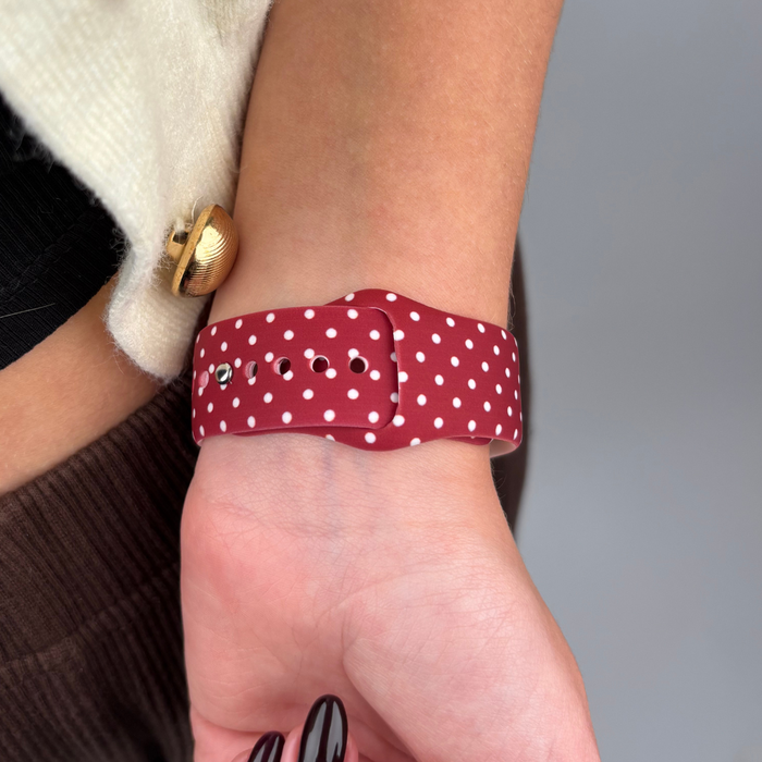 Burgundy polka dot Apple Watch strap on wrist next to beige coat with a gold button.
