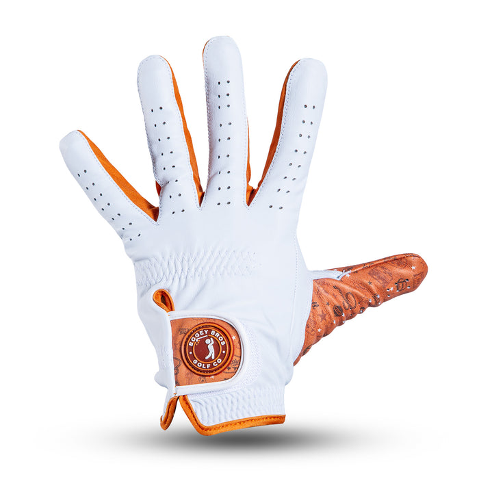 A white golf glove with orange trim and accents is displayed palm-up. The glove features small perforations for breathability, a circular logo patch on the wrist, and textured material on the thumb and lower palm. The background is plain white.