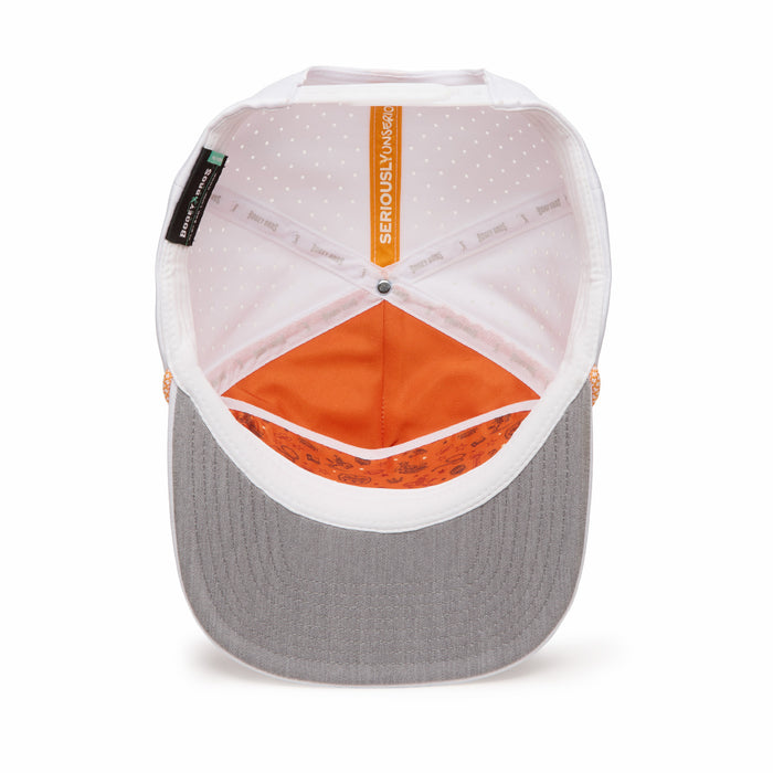 A top-down view of the inside of a baseball cap with a grey brim, white crown, orange inner lining, white polka-dot pattern, and a visible “SERIOUSLY SNACKS” label at the top. The sweatband has repeating branding and small designs near the brim.