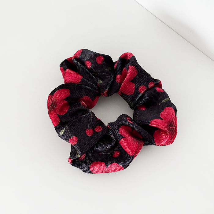 Red scrunchie with cherry pattern by Coconut Lane on a white surface.