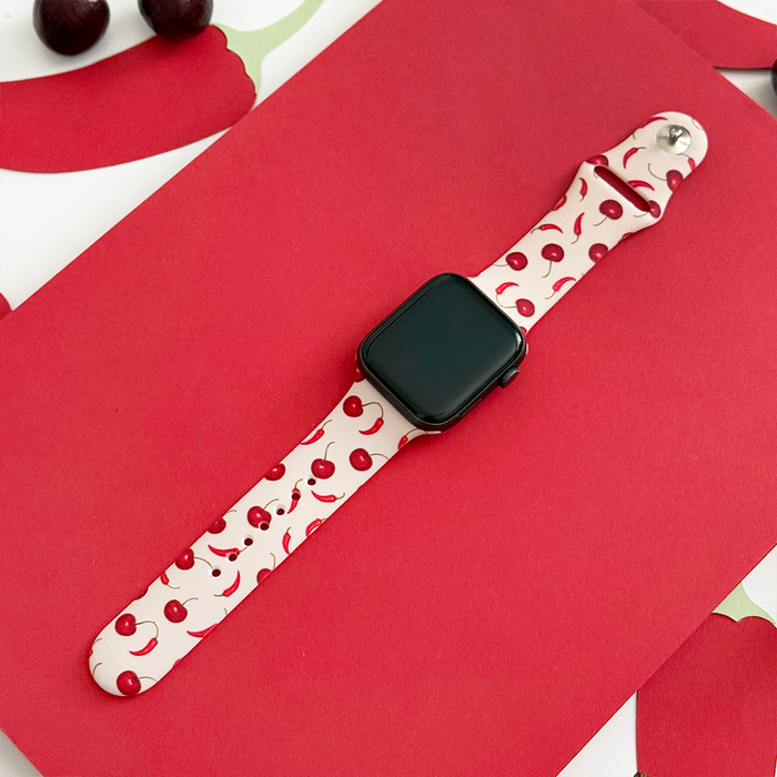 Cherry Spice Apple Watch strap by Coconut Lane on a red surface with cherries beside it.
