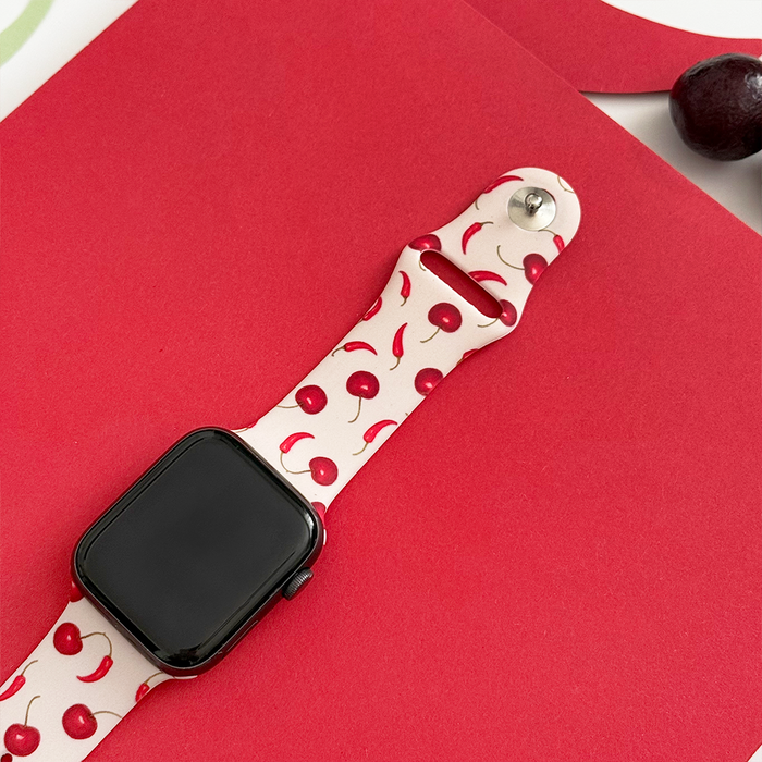 Red Coconut Lane Cherry Spice Apple Watch strap with cherry pattern, shown beside a dark cherry.