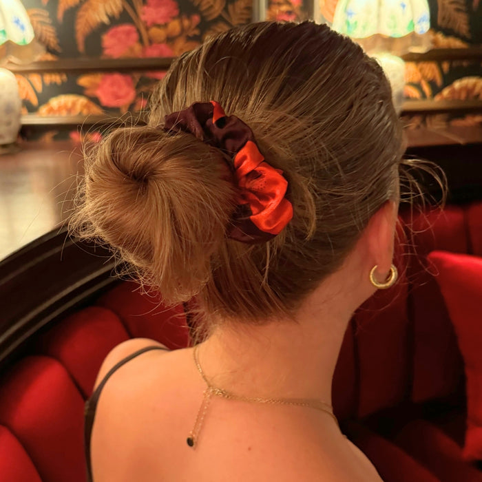 Woman with light brown hair in a bun wearing a Cinnamon Lily scrunchie, sitting on a red velvet couch.
