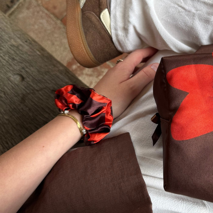 Cinnamon-colored scrunchie with a gold bracelet beside a brown pouch featuring a red heart print.