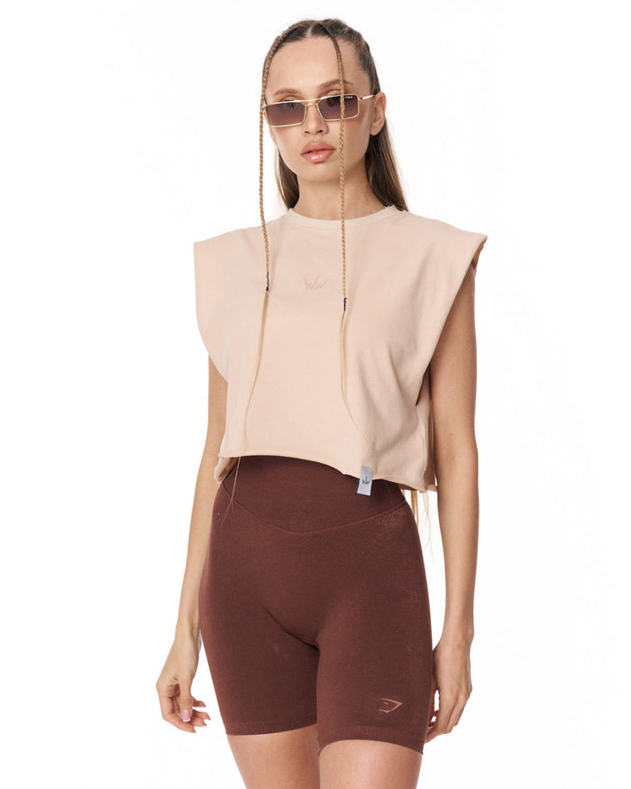 A model wearing a light beige sleeveless crop top and dark brown fitted biker shorts against a plain white background.