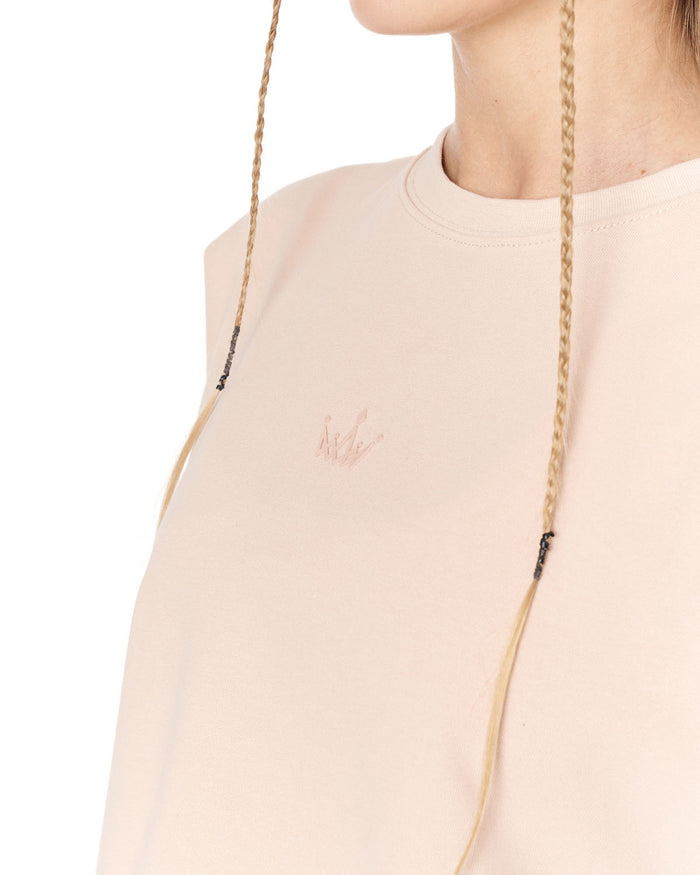 Close-up of a person wearing a pale blush pink crewneck sweatshirt with a small tonal embroidered logo on the chest and braided drawstrings.