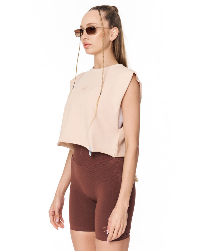 A woman modeling a sleeveless cropped top in light beige and matching brown fitted shorts against a plain white background.