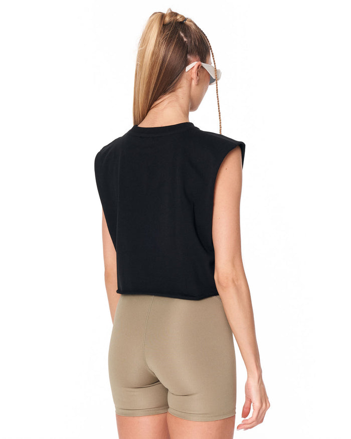 A woman shown from the back wearing a black sleeveless crop top and beige fitted shorts against a plain white studio background.