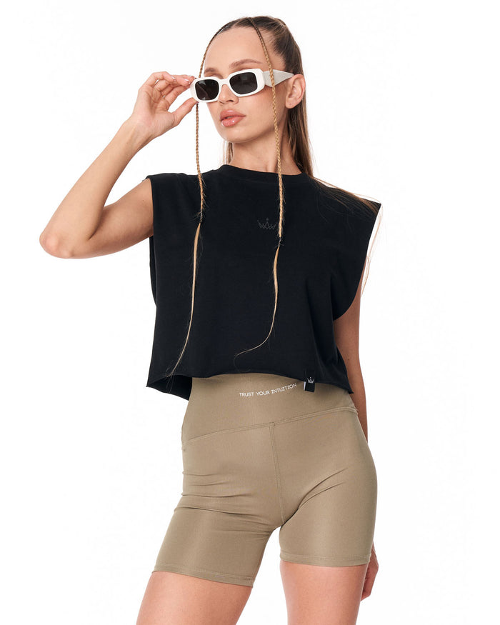 A woman modeling a black sleeveless crop top and beige fitted biker shorts against a plain white background.