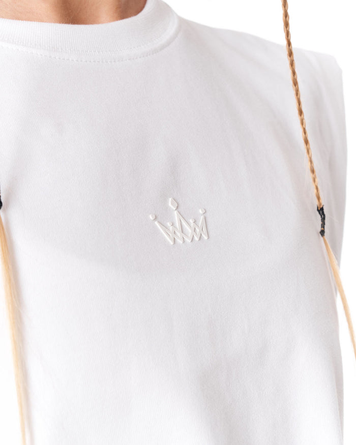 Close-up of a white crewneck t-shirt featuring a small white embroidered crown logo on the chest, worn by a model with a braided blonde ponytail visible on the right side.
