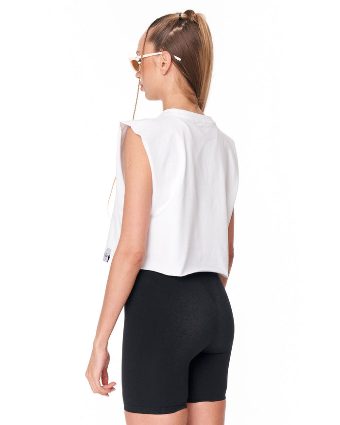A woman shown from the back wearing a white sleeveless cropped top and black fitted biker shorts against a plain white studio background.
