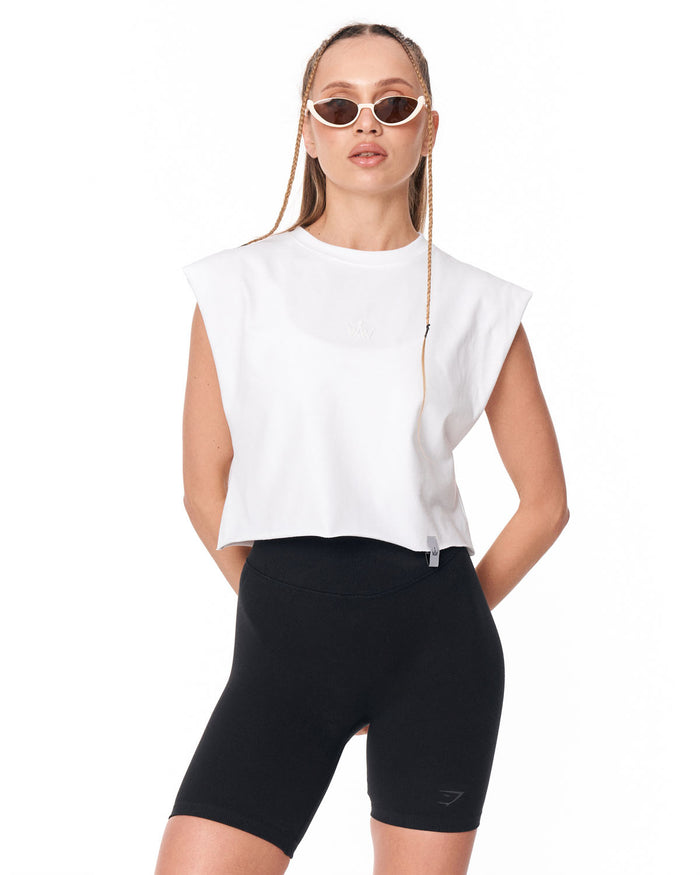 A woman modeling a white sleeveless crop top and black biker shorts against a plain white background.