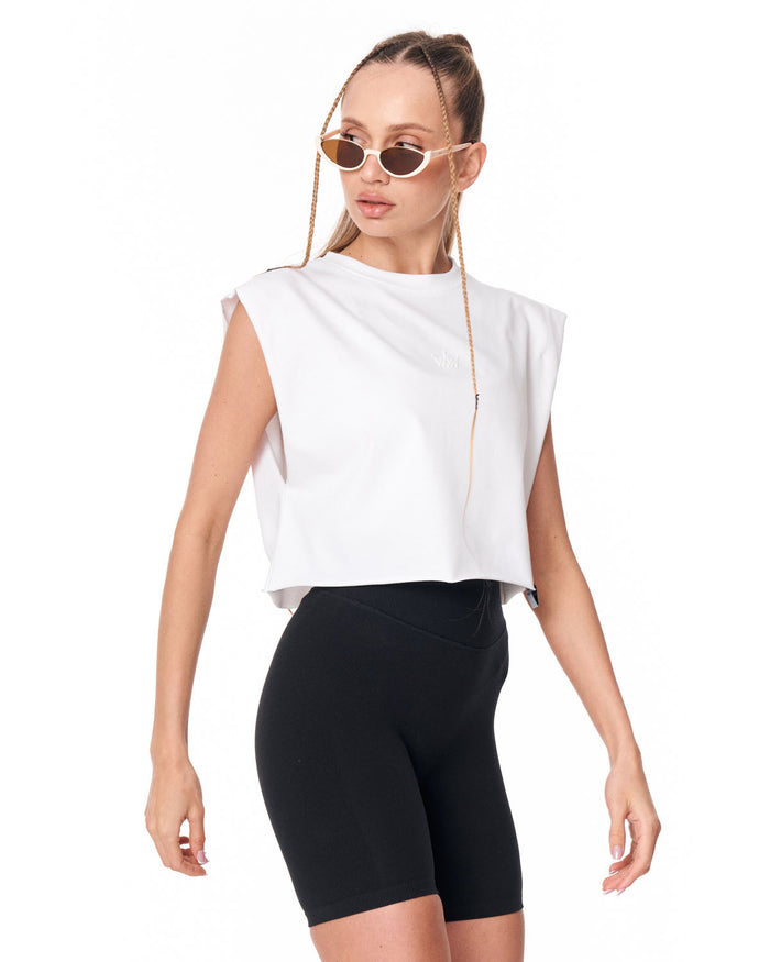 A woman modeling a white sleeveless cropped top and black fitted biker shorts against a plain white studio background.