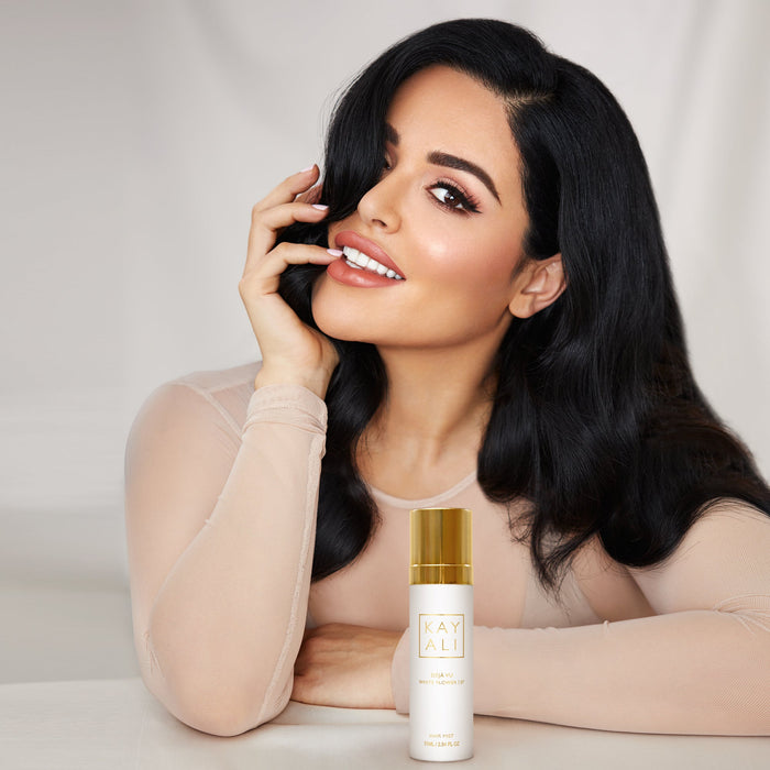Woman with long black hair and a bottle of kayali product on a light background