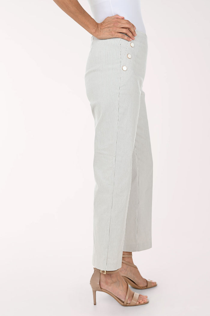 A model wearing light sage green pinstriped trousers with decorative gold buttons on the sides, paired with beige strappy high-heeled sandals against a plain white background.