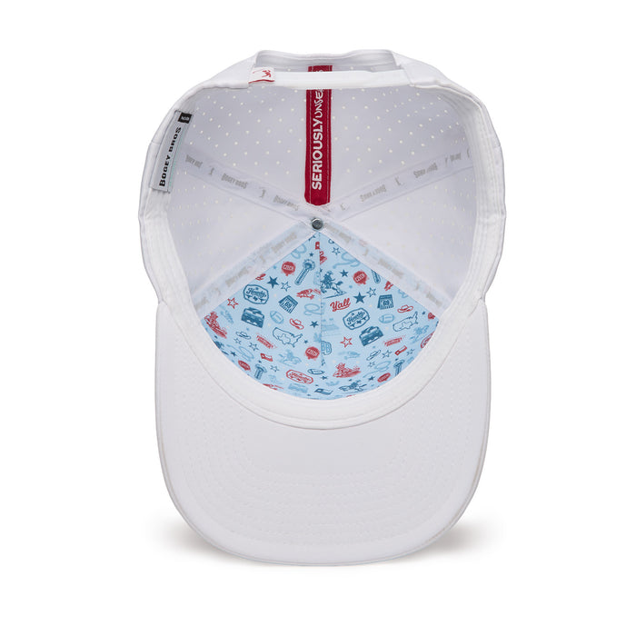 The underside of a white baseball cap is shown. The front interior is light blue with playful, multicolored prints of summer-themed icons such as sunglasses, palm trees, and sailboats. The rest of the interior is white with small dots and fabric tags along the band.