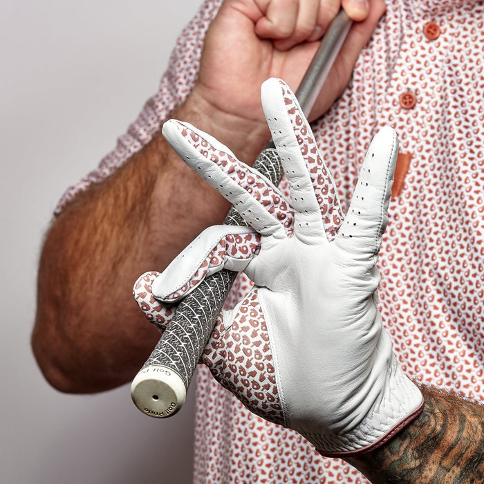 A person wearing a patterned golf shirt and the Get In The Hole - Glove holds a club, their gloved hand making an "OK" gesture. Tattoos are visible on their arm and the club rests in the palm of the Get In The Hole - Glove.