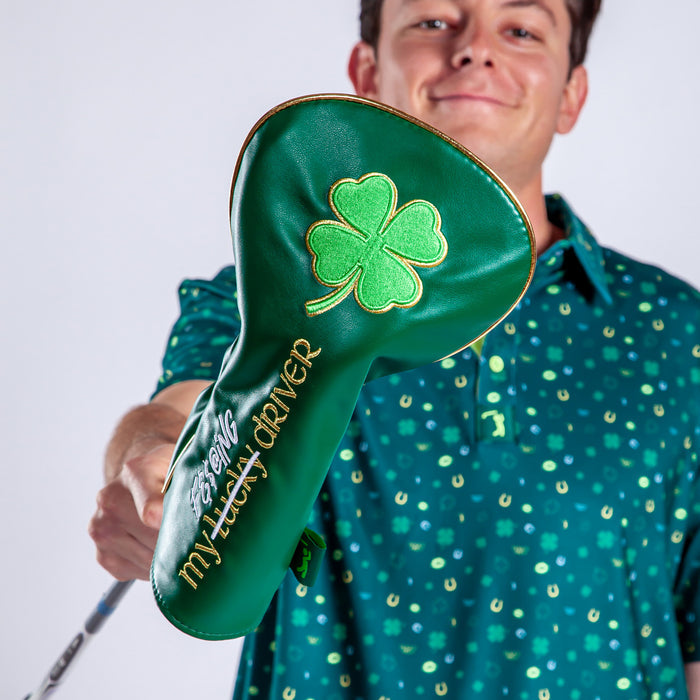 A smiling man in a green horseshoe-patterned shirt holds out the Gettin' Lucky - Driver Headcover, made of premium PU leather with an embroidered bright green four-leaf clover and gold "This is my lucky driver" text, against a white background.