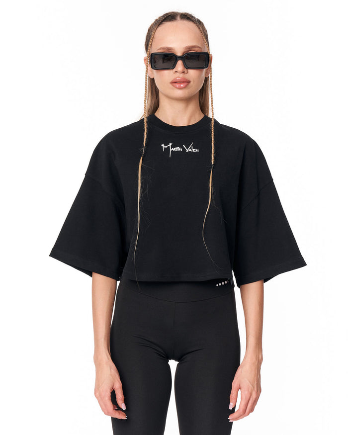 A model wearing a black cropped t-shirt with a white 'Martin Valen' logo on the chest, paired with black leggings and black sunglasses, against a plain white background.