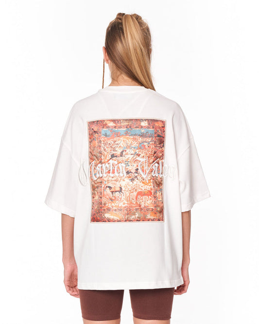 A woman viewed from behind wearing an oversized white t-shirt with a large, detailed vintage-style map graphic on the back in shades of red, orange, and blue, paired with brown shorts against a white background.