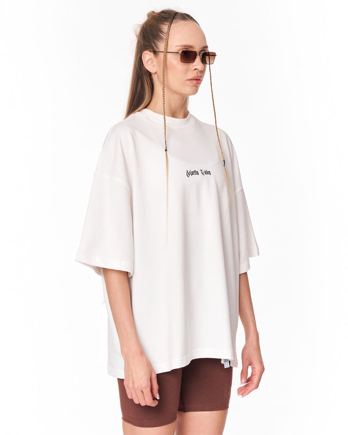 A woman modeling an oversized white short-sleeve T-shirt with a small black 'Palm Angels' logo on the chest, paired with brown shorts and sunglasses, against a plain white background.