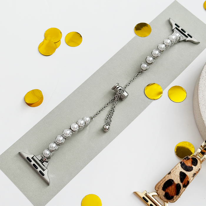 Silver Isla Pearl Apple Watch strap by Coconut Lane displayed on a gray strip with yellow confetti and leopard print band.