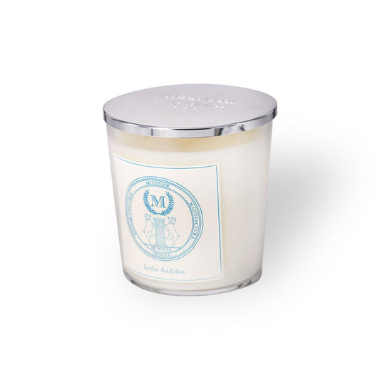 A white candle in a glass container with a silver lid, featuring a blue label that reads "Jardin Andalou."