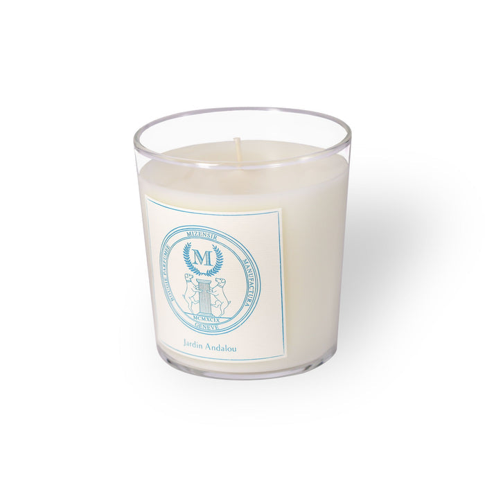 A white candle in a clear glass container featuring a decorative label with a blue emblem and the text "Jardin Andalou."