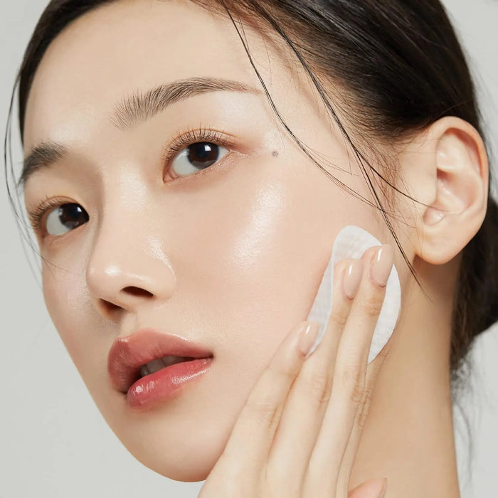 Woman applying cream to her face with a neutral background